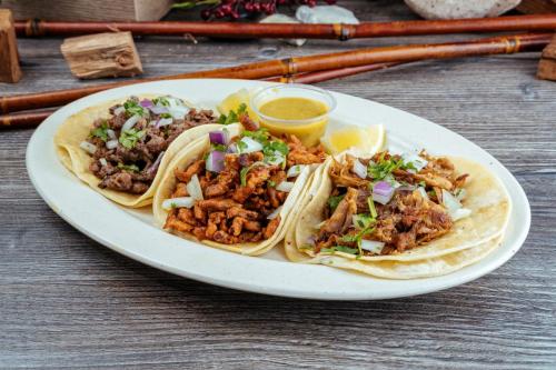 Three tacos on a plate: grilled beef (asada), chicken, and carnitas, served with fresh toppings